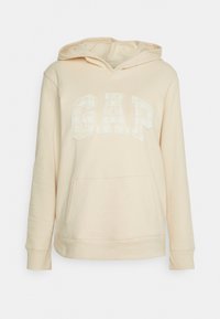 Crèmekleurige hoodie gemaakt van zacht materiaal; heeft een voorzak en een "GAP"-logo met een geblokt patroon.