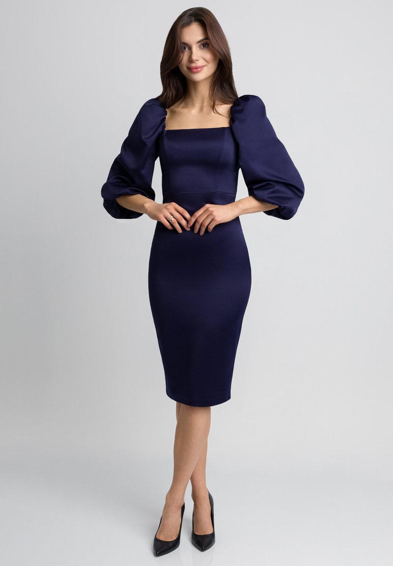 Granatowa, dopasowana sukienka z kwadratowym dekoltem, puffami w długości łokcia i gładką teksturą, w połączeniu z czarnymi szpilkami.