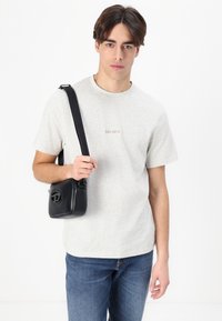 T-shirt grigio a maniche corte con la scritta "LES DEUX", jeans blu e una piccola borsa a tracolla in pelle nera con un dettaglio circolare in metallo.