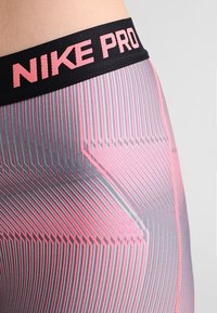 Los leggins Nike Pro cuentan con una cintura negra con el logo en rosa, un patrón a rayas en gris y rosa, y un tejido suave y elástico.