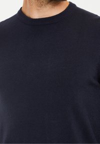 Pull tricoté bleu marine avec un col rond côtelé et une texture lisse. Le tissu présente un design uniforme sans motifs.