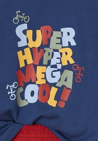 Bunte Blockbuchstaben auf blauer Stoffoberfläche bilden "SUPER HYPER MEGA COOL!" mit kleinen Fahrrad-Icons in Gelb, Weiß und Rot rund um den Text.