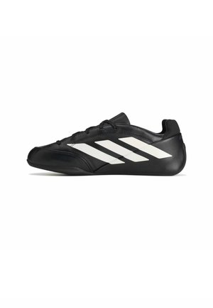 Chaussure de sport noire profil bas avec des bandes diagonales blanches sur le côté et des lacets noirs, vue de l'extérieur sur fond blanc.