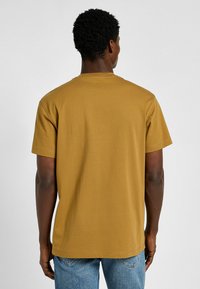 Senfgelbes Baumwoll-T-Shirt mit kurzen Ärmeln, Rundhalsausschnitt und lockerer Passform. Schlichtes Design, keine sichtbaren Muster oder Logos.