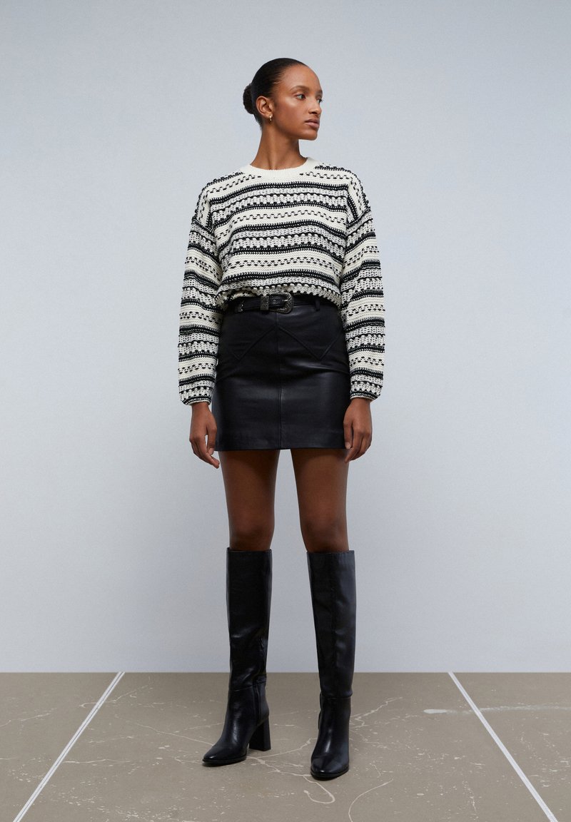 Pull en tricot avec des rayures horizontales noires et blanches, associé à une jupe mini en cuir noir et des bottes en cuir noires jusqu'aux genoux.