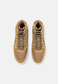 Ett par tan- och svarta hög-top kvalitetsskor med vita sulor och mönstrade snören, sett ovanifrån mot en vit bakgrund.