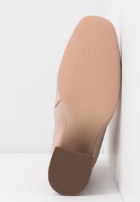 Chaussure à talon haut couleur nude avec une tige en matériau lisse et une semelle en caoutchouc texturée. Taille 38 indiquée sous la chaussure.