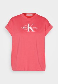 Koralo spalvos medvilnės marškinėliai su trumpomis sukeltomis rankovėmis, ant priekio esantis baltas tekstas: "Calvin Klein Jeans" ir didelis baltas "CK" logotipas.