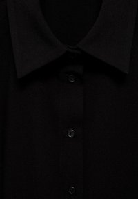 Camicia nera con colletto classico, quattro bottoni e tessuto testurizzato. Il design è elegante e minimalista.