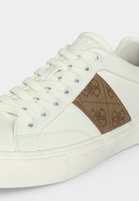 Baskets basses blanches avec lacets blancs, un panneau latéral marron texturé avec un motif subtil, et une semelle en caoutchouc blanche.