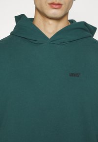 Sudadera verde hecha de algodón con una textura suave. Cuenta con un bolsillo canguro frontal y un pequeño logo negro de Levi's en el pecho.