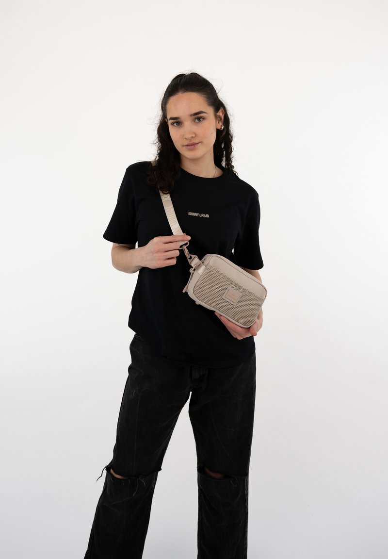 Borsa a tracolla beige con motivo testurizzato, tracolla regolabile e scomparti con zip, indossata da una persona con una maglietta nera e jeans strappati.