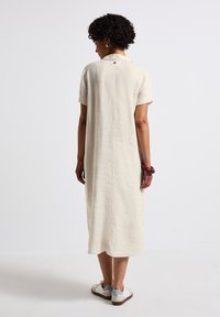 Vestito in lino color crema con maniche corte, colletto con bottoni e silhouette dritta. Indossato con sneakers bicolore.