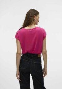 Fuchsia kortärmige top gemaakt van zachte stof, met een ronde halslijn en een ontspannen pasvorm, gecombineerd met hoogwaisted donkerdenim jeans.
