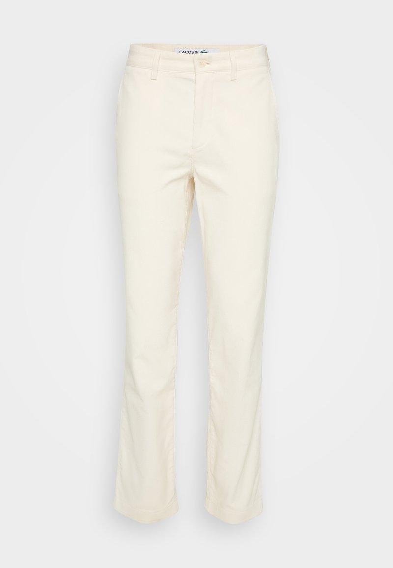 Pantalon beige slim avec passants pour ceinture, fermeture devant par bouton et zip, et poches latérales, présenté sur fond blanc.