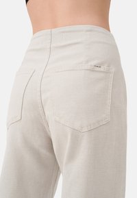 Lichtbeige wijde broek van textuurstof met een hoge taille, voorzien van twee achterzakken en een klein merklabel op de rechter zak.