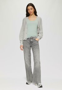 Lichtgrijze gebreide cardigan met knopen over een mintgroene tanktop, gecombineerd met hoogwaisted grijze denim flared broeken en gestreepte sneakers.