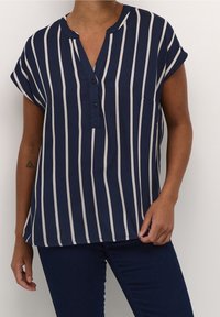 Blouse à rayures bleu marine avec manches courtes, un col en V, des boutons à l'avant et une poche. Les rayures sont de couleur crème et régulièrement espacées. Texture lisse.