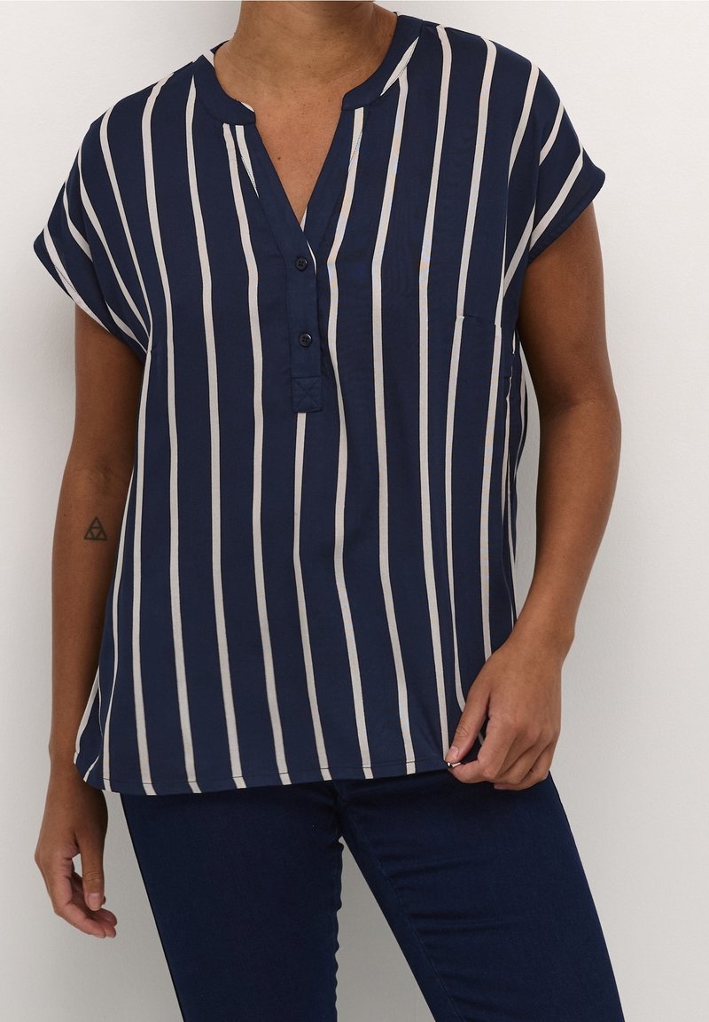 Blouse à rayures bleu marine avec manches courtes, un col en V, des boutons à l'avant et une poche. Les rayures sont de couleur crème et régulièrement espacées. Texture lisse.
