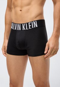 Black boxer briefs made of smooth fabric with a wide white Calvin Klein logo waistband. Features a fitted design and short leg length.