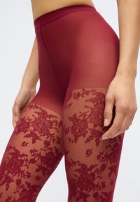 Bordeauxfarbene Leggings mit einem durchsichtigen, floralen Spitzenmuster an den Unterschenkeln, einem glatten oberen Abschnitt und einem bequemen breiten Bund.