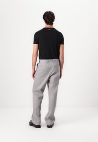 Schwarzes Kurzarmhemd und hellgraue gefaltete Hose mit Gesäßtaschen, vor einem schlichten weißen Hintergrund.