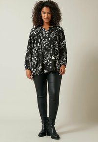 Blusa a maniche lunghe a fantasia bianca e nera con pieghe, abbinata a leggings neri in ecopelle e stivaletti. Texture liscia in tutto il capo.