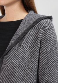 Cardigan gris con capucha, patrón de espiga, tejido texturizado y ribete oscuro en contraste a lo largo del cuello.