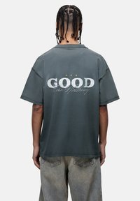 Donkergrijze oversized t-shirt met korte mouwen. Grafische tekst "GOOD" en "for Nothing" op de achterkant, met daarboven drie sterren in lichte kleuren.
