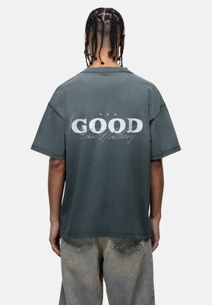 T-shirt oversize grigio scuro con maniche corte. Grafica con testo "GOOD" e "for Nothing" sulla parte posteriore, con tre stelle sopra in colori chiari.