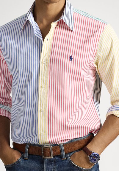 Πουκάμισο με γιακά και πολύχρωμες κάθετες ρίγες σε μπλε, κόκκινο, κίτρινο και λευκό. Περιλαμβάνει ένα μικρό κεντητό λογότυπο και κουμπιά.