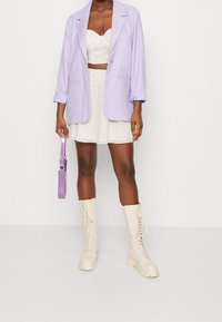 Lavendel oversized blazer, vit blommig crop top, utsvängd minikjol, kombinerat med knähöga beige snörstövlar och en lavendelväska.