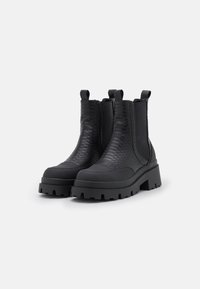 Bottines noires avec un motif en cuir serpent texturé, des panneaux latéraux élastiques et des semelles épaisses à crampons pour une meilleure adhérence et stabilité.