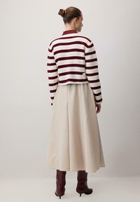 Crochetovaný maroon a bílý pruhovaný svetr s límcem, kombinovaný s plnou bílou sukní a burgundskými kozačkami po kolena. Dvě zlaté knoflíky viditelné.