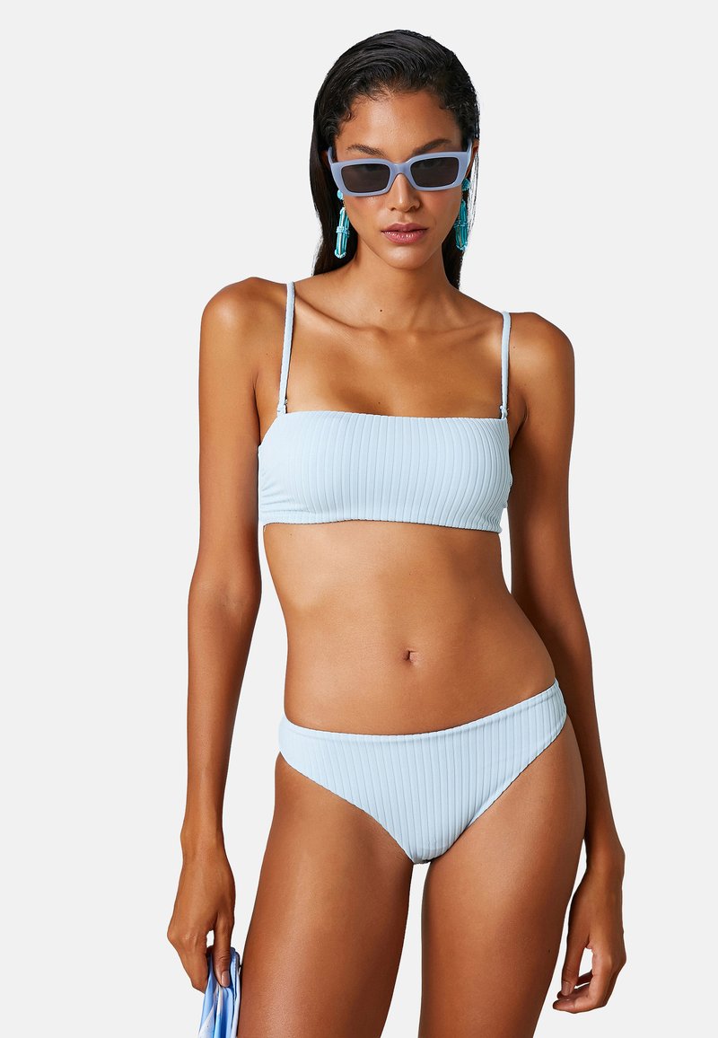 Jasnoniebieski, prążkowany bikini z topem bandeau i wysokim stanem majtek. Posiada cienkie ramiączka i miękką teksturę. Bez dodatkowych wzorów czy akcentów.