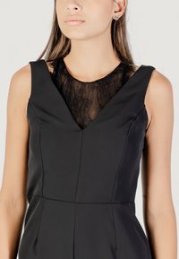 Vestido negro sin mangas con un diseño de escote en V. El corpiño tiene un encaje en la parte del escote, creando un contraste texturizado.