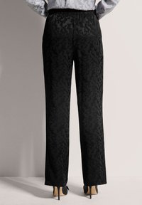 Zwarte broek met een matte afwerking, voorzien van een subtiel textuurpatroon. Langwerpig recht ontwerp en een elastische tailleband voor comfort.