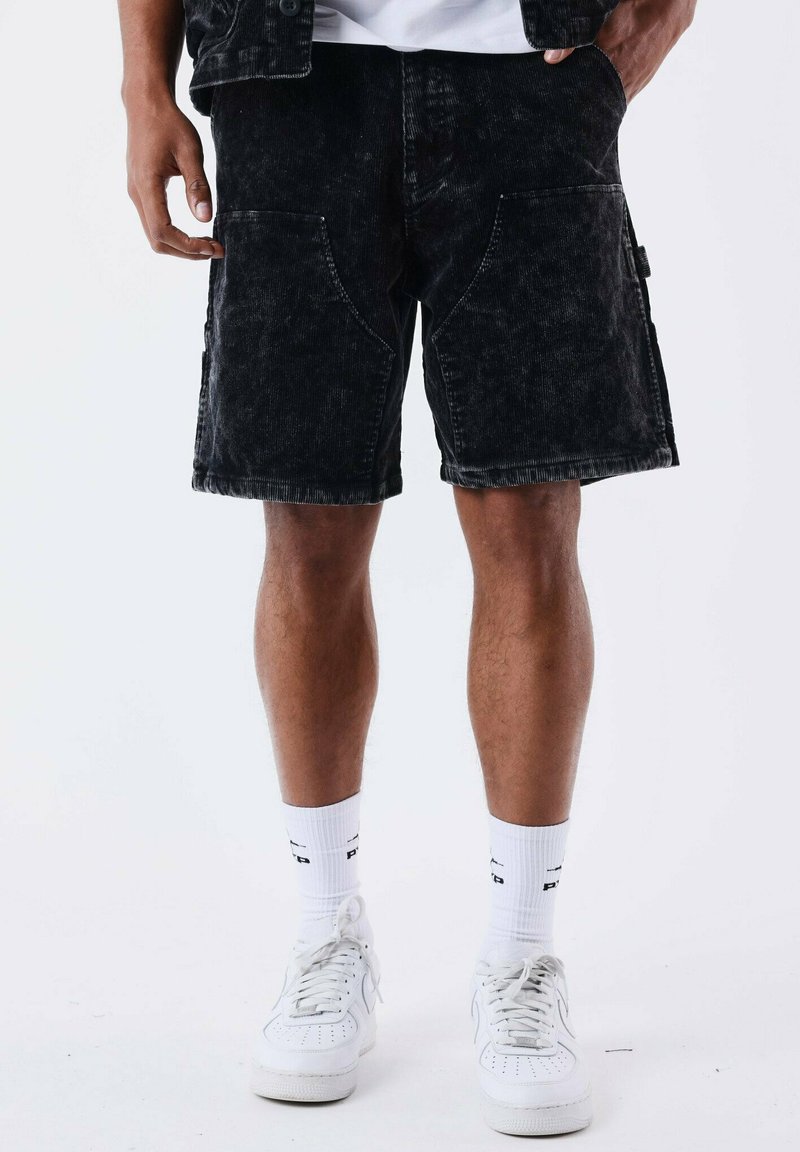 Shorts en denim noir avec une texture délavée, dotés de poches latérales et d'une coupe droite, accompagnés de baskets blanches et de chaussettes.