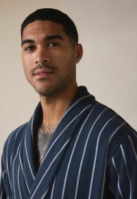 Jūras izmēra striķis, kas izgatavots no mīksta auduma ar šaura apkakli, ar baltām vertikālām svītrām un brīvu piegriezumu.