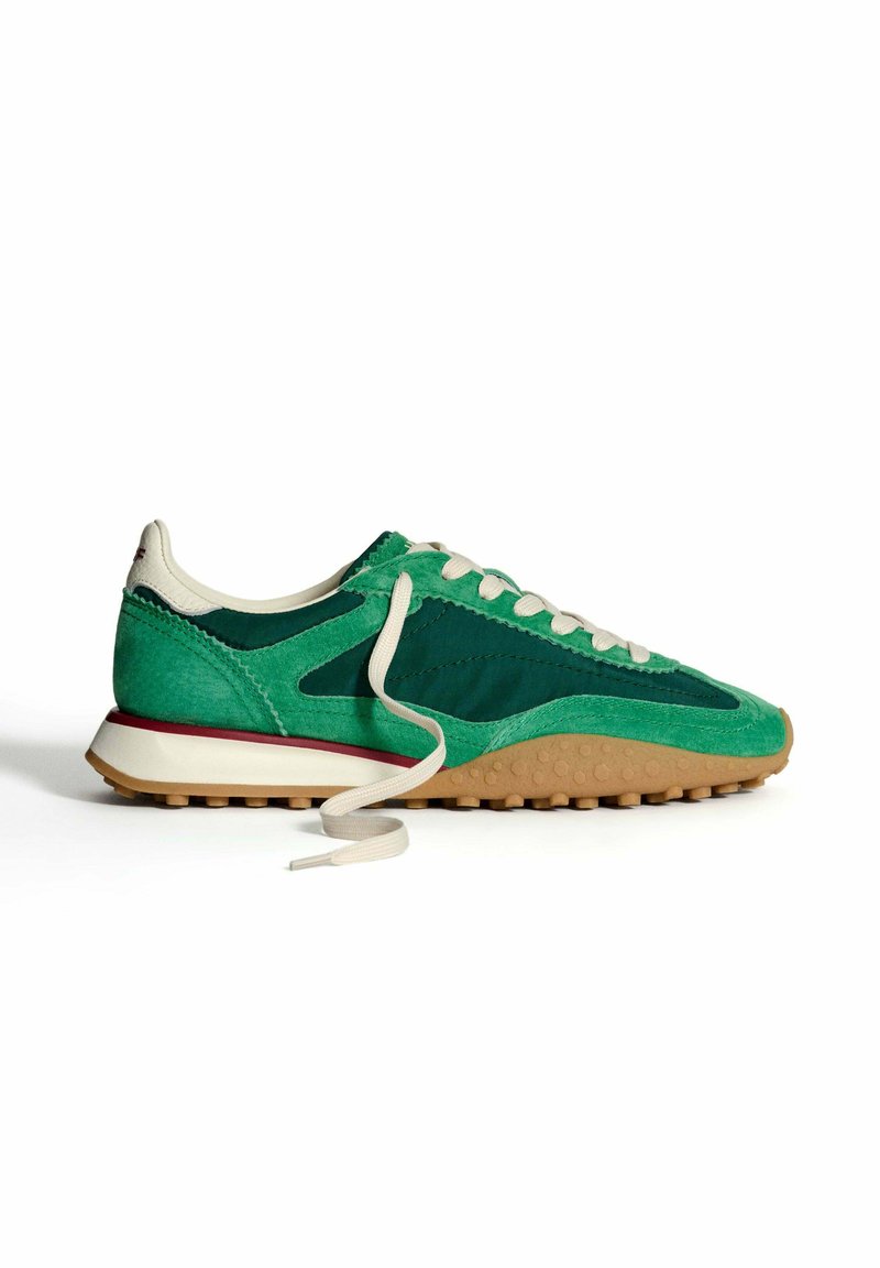 Sneaker verde in suede e tessuto con lacci crema, suola in gomma e un'intersuola tessurizzata. Presenta un design a strati e accenti a contrasto.