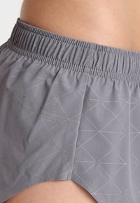 Grå löp短byxor med elastisk midja; har ett geometriskt mönster och varumärkestext på tyget. Lättviktsmaterial, slät textur.