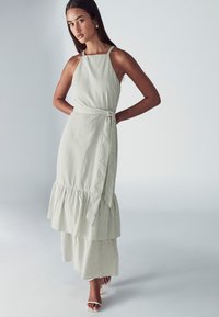 Juostuota, be rankovių suknelė šviesiai žaliai ir balta spalvomis, su rauktu, sluoksniuotu sijonu ir surišta juosmens detale. Lygi medžiaga, laisvas dizainas.