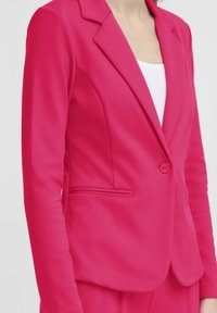 Fitted roze blazer met een enkele knoopsluiting, met gekartelde revers en zijzakken, gemaakt van een gladde stof met een minimale textuur.