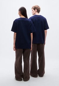 Μπλε ναυτικό βαμβακερά μπλουζάκια σε μεγάλα μεγέθη, φορεμένα με φαρδιά καφέ παντελόνια, από πίσω. Απλός σχεδιασμός με στρογγυλή λαιμόκοψη και κοντά μανίκια.