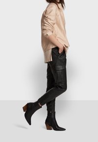 Beige, lätt långärmad skjorta, matchad med svarta läder cargo-byxor med fickor, samt svarta spetsiga ankelstövlar med bruna klackar.