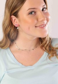 Silberne, sternförmige Ohrringe und eine passende silberne Sternhalskette. Das Model trägt ein hellblaues V-Ausschnitt-Oberteil und hat welliges Haar.