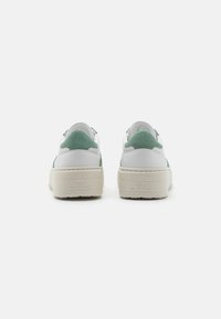 Hvite sneakers med lysegrønne semskede detaljer, rund form, minimalistisk design, med en tykk kremfarget såle og preget merke.