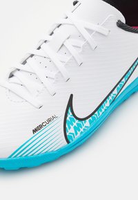 Scarpa da calcio Nike Mercurial bianca presenta una tomaia testurizzata, accenti neri e dettagli turchesi con un motivo unico sulla suola.