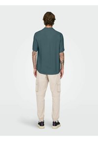 Short-sleeve, teal shirt with a collar, relaxed fit. Paired with beige cargo pants featuring side pockets and cuffs. Black sneakers with purple accents.