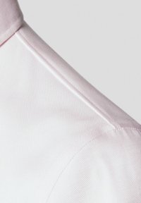 Jasnoróżowy kołnierzyk koszuli z drobną teksturą prążkową, gładkim wykończeniem i starannie zszytymi brzegami. Skupienie na szczegółach tkaniny i koloru.